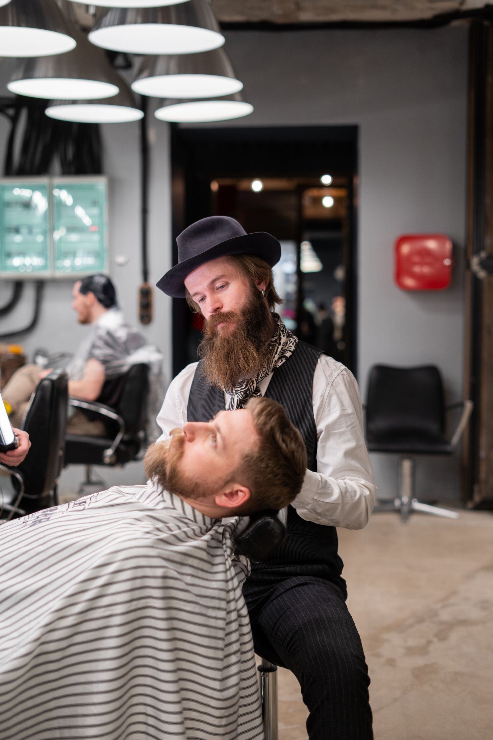 Barber working over a reclined client under the shop lamps