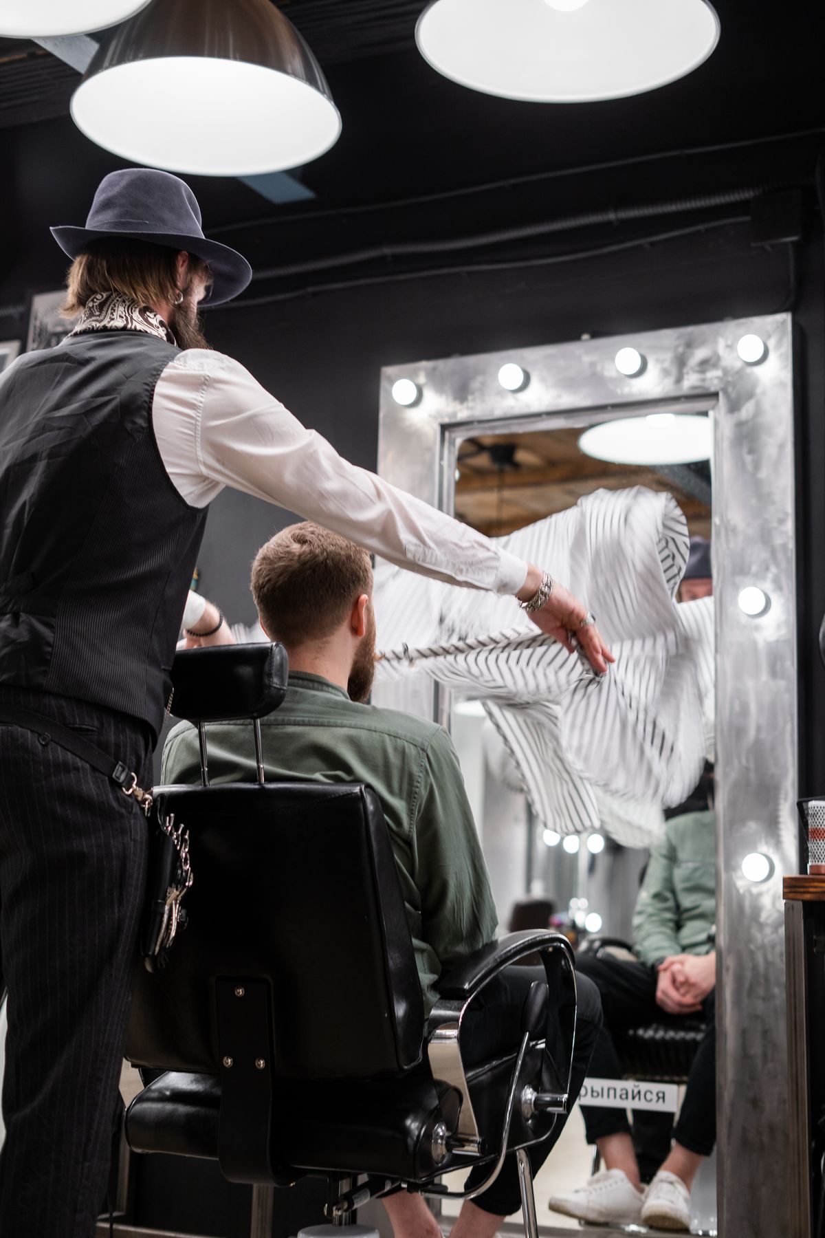 Barber finishing a client at a mirror-lit station